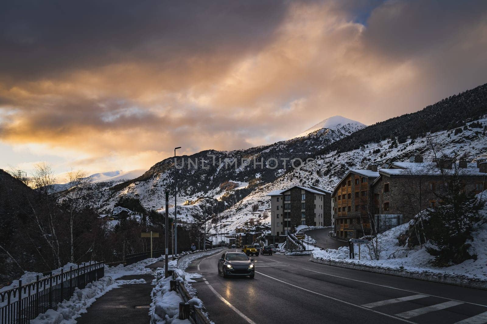 Cars on the road leading to El Tarter village after dusk. Sunset with sunlight illuminating mountain peaks in Pyrenees mountains, Grandvalira, Andorra
