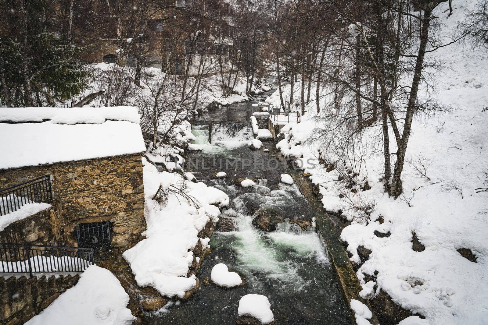 Valira dOrient river in winter with snow banks in El Tarter mountain village in Pyrenees Mountains, Grandvalira, Andorra