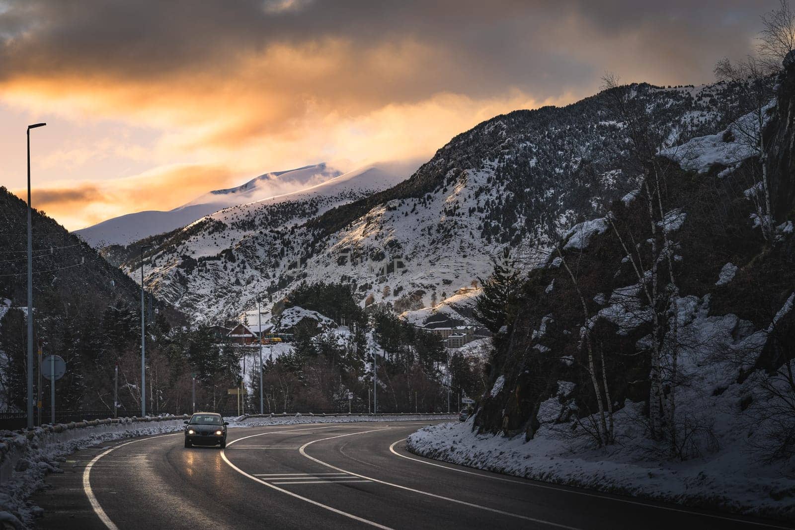 Car on the road leading to El Tarter village after dusk. Sunset with sunlight illuminating mountain peaks in Pyrenees mountains, Grandvalira, Andorra