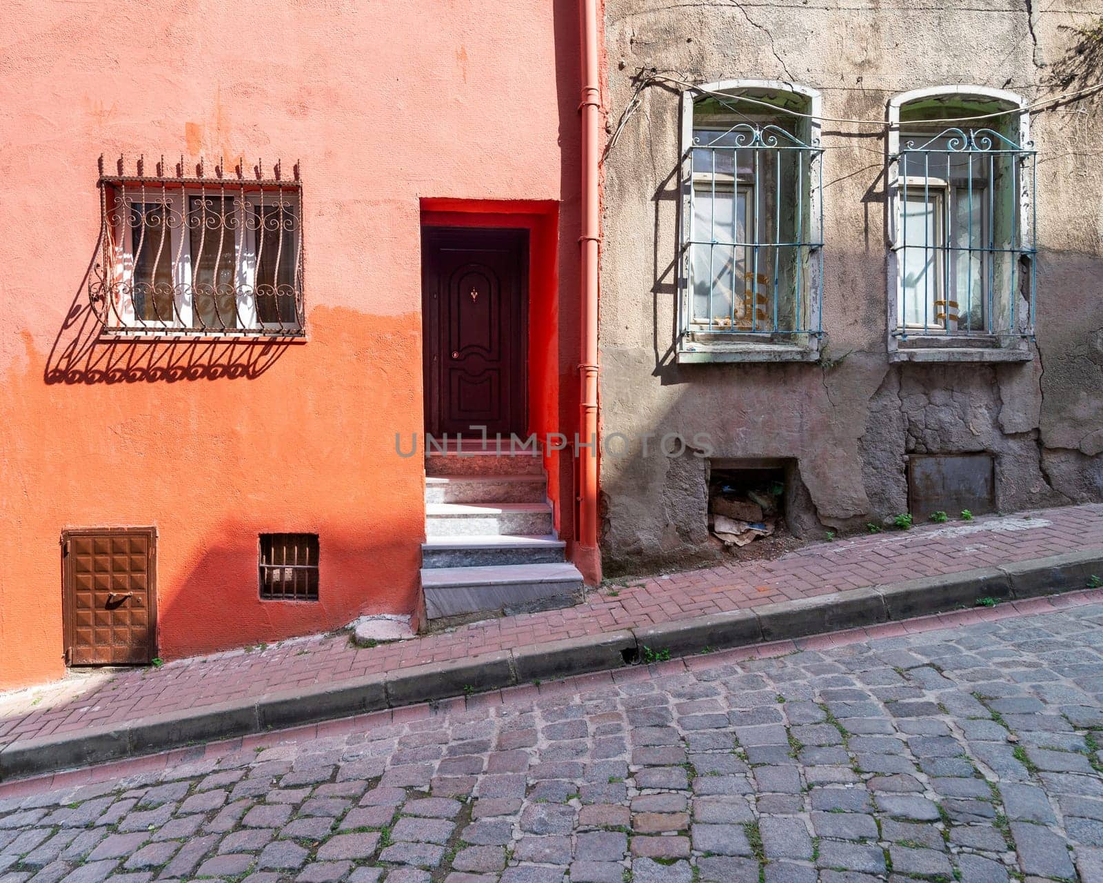 Exterior facade of old residential building with walls painted in orange, and wrought iron windows, at a narrow cobblestone street, Balat district, Istanbul, Turkey