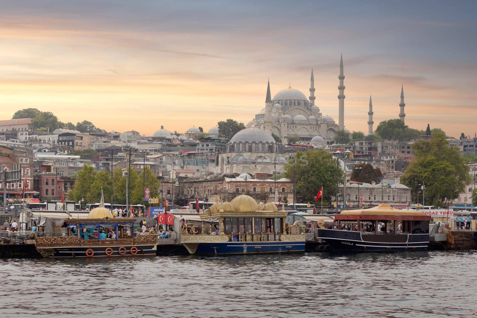 Istanbul, Turkey - August 25, 2022: Traditional fast food bobbing boats serving fish sandwiches at Eminonu square with Rustem Pasha Mosque and Suleymaniye Mosque in the background before sunset