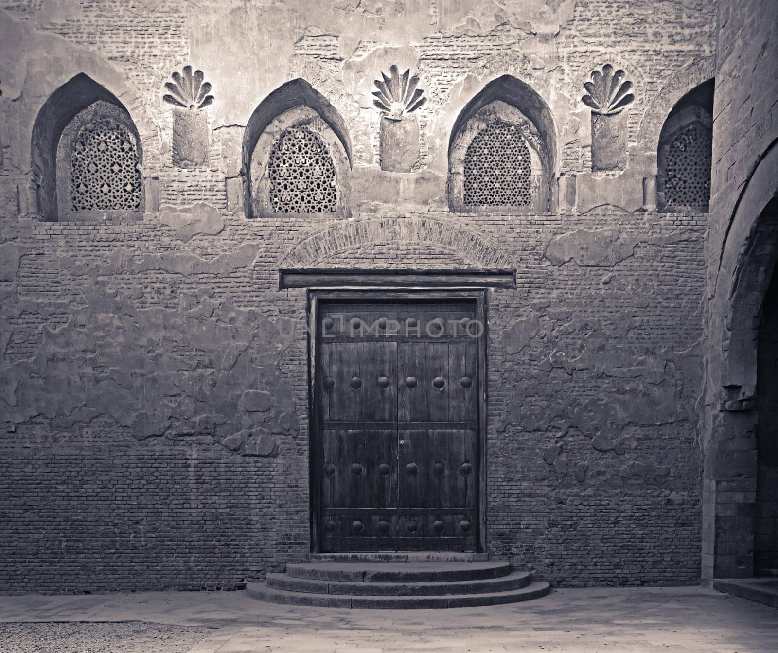 Aged wooden weathered door, perforated arched stucco window decorated with floral patterns, and three steps on stone bricks wall, Ibn Tulun Mosque, Cairo, Egypt