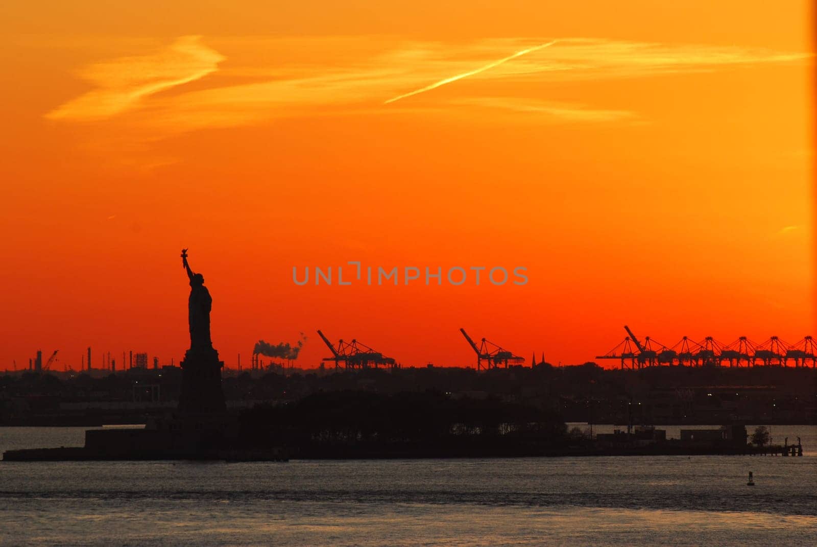 Silhouette of Statue of Liberty and Liberty Island in New York against an orange sunset sky