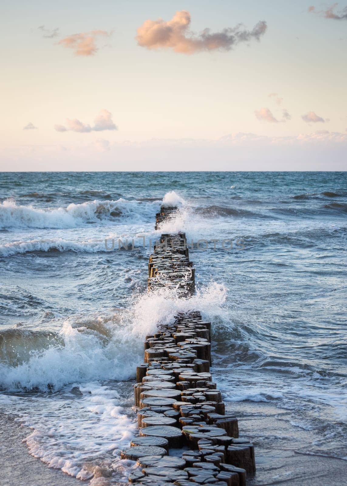 Stormy waves of the Baltic sea under the sun rays in evening. View from the sandy shore