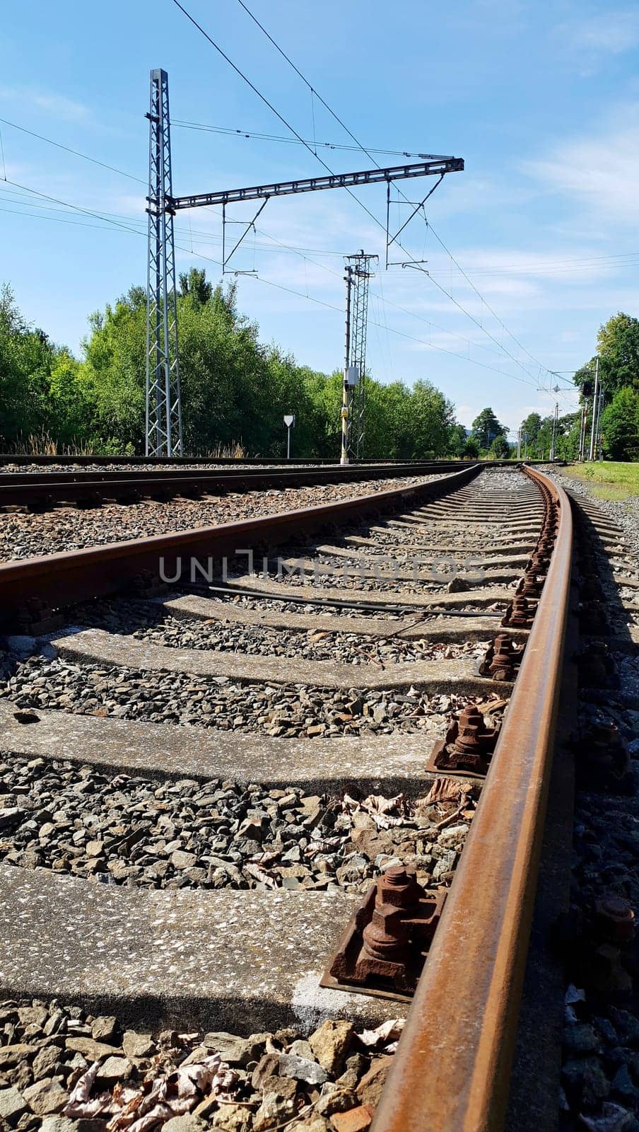 Empty railway rusty train tracks closeup. View of electrified country track with blue sky.
