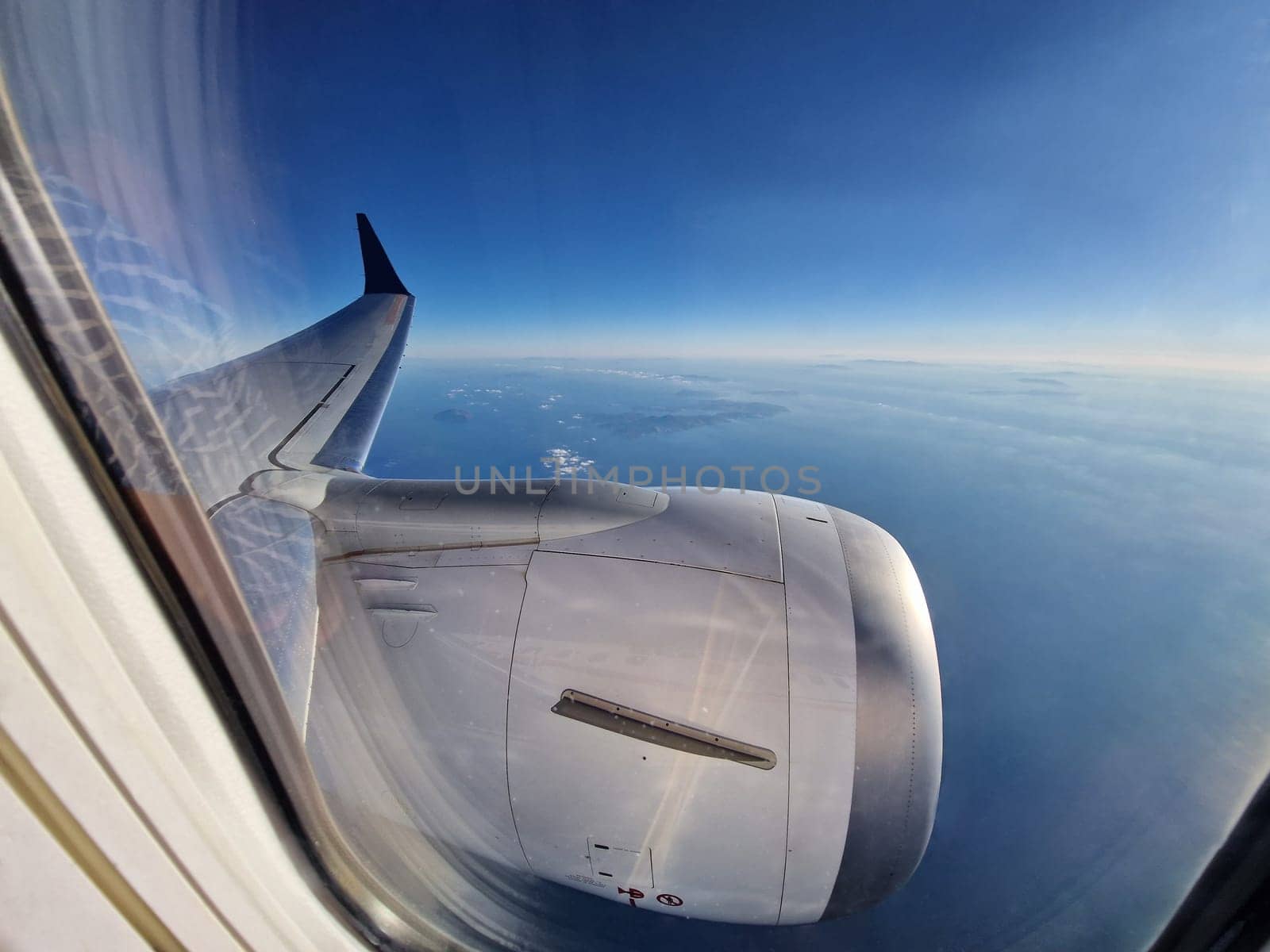 A view of blue sky through airplane window during flight. View from airplane window with wing and engine during flight in the air.