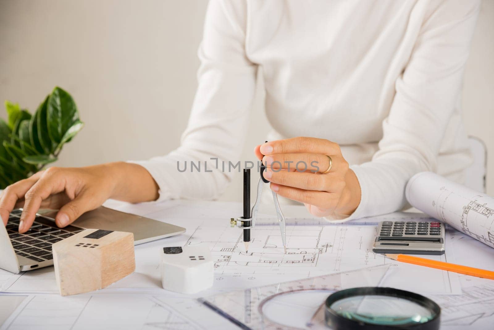Architectural project workplace. Architect typing laptop keyboard to review design of house before editing or sketching with compass on plan blueprint paper on table desk at architecture office