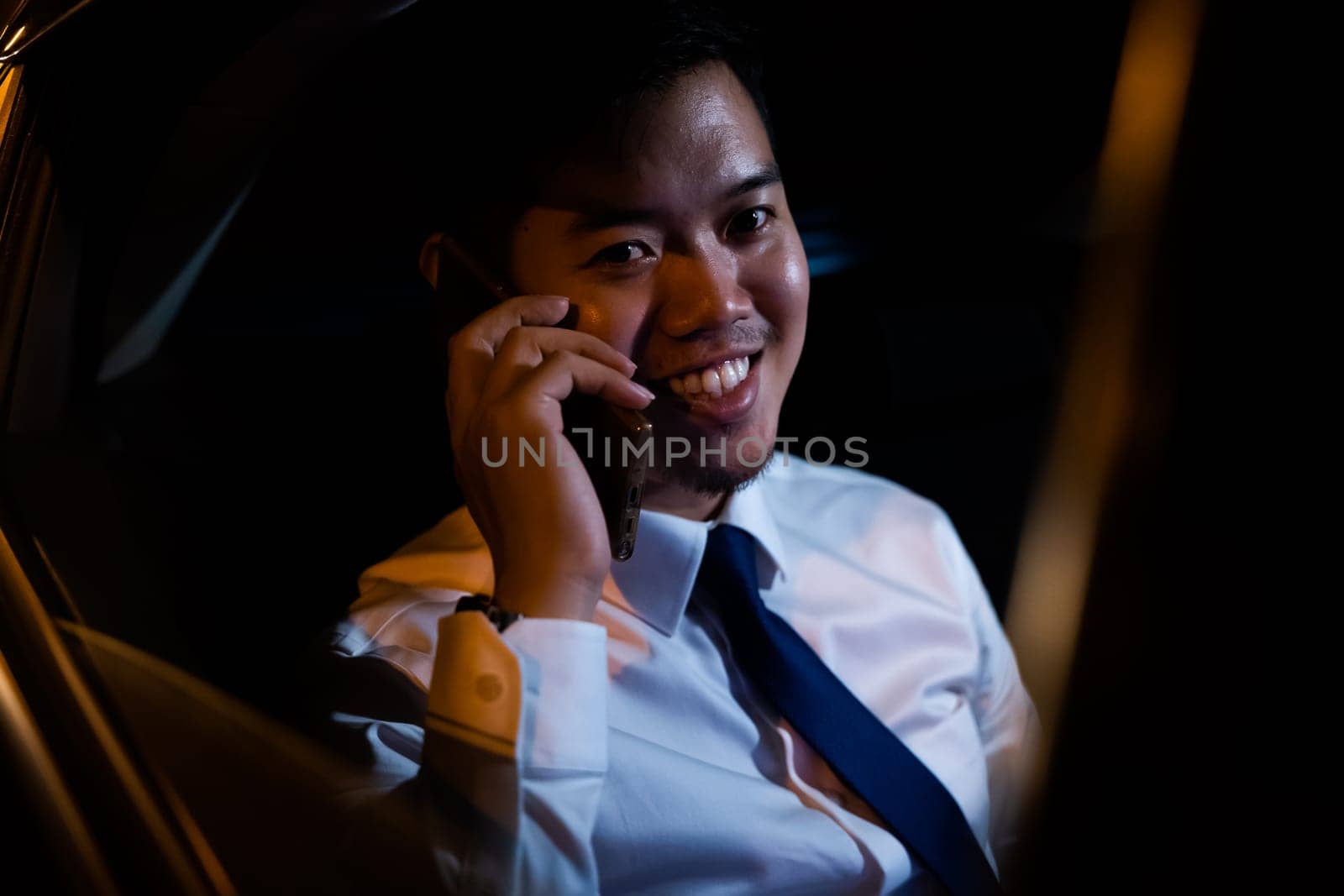 Businessman using smartphone in backseat of car near window at night, Handsome Asian young man work on late night sitting back seat and still work with mobile phone in city street