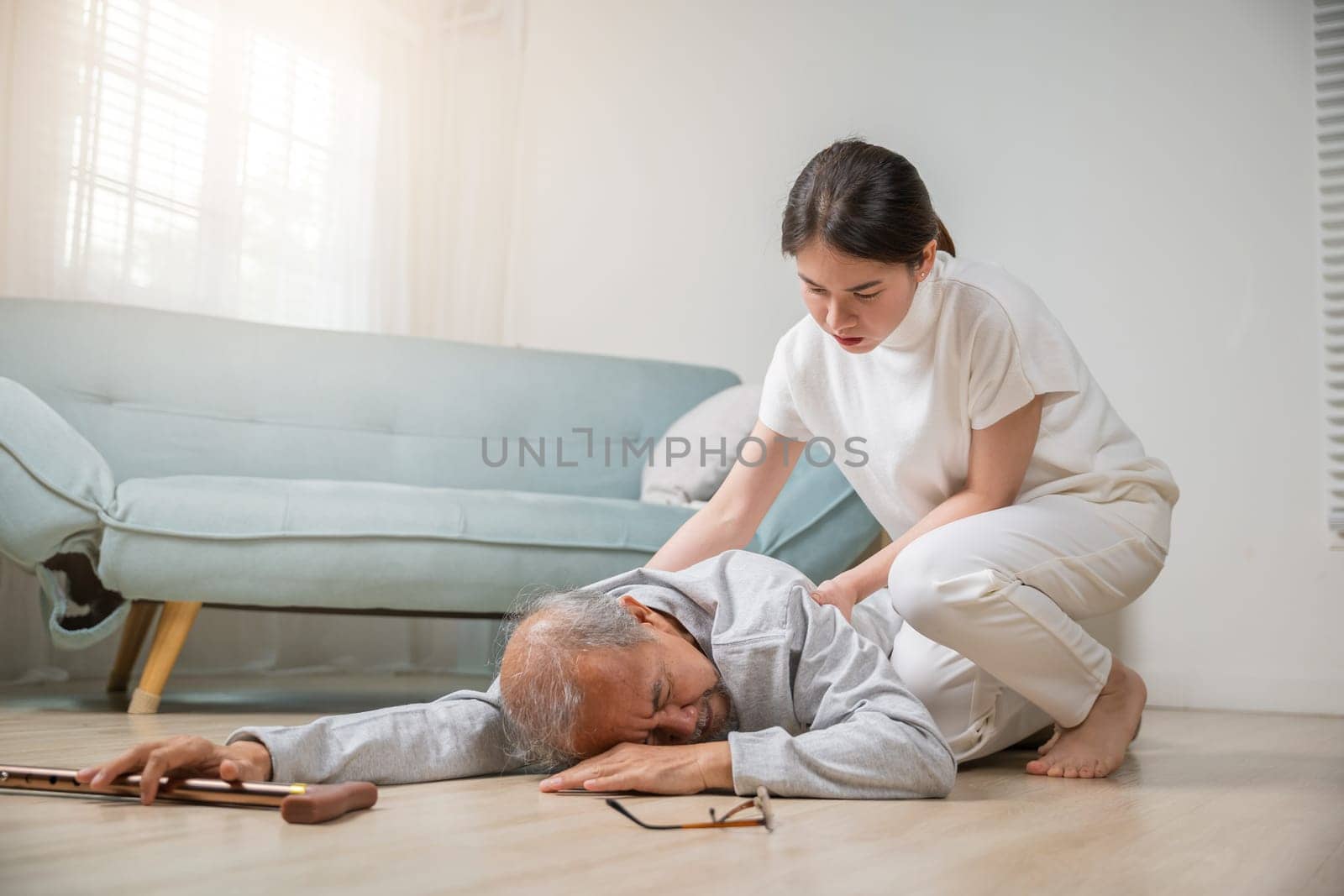 Asian elderly old man with walking stick fall on ground and granddaughter camp to help to support at home in living room, young woman halping her grandfather after falling down on floor, dizziness