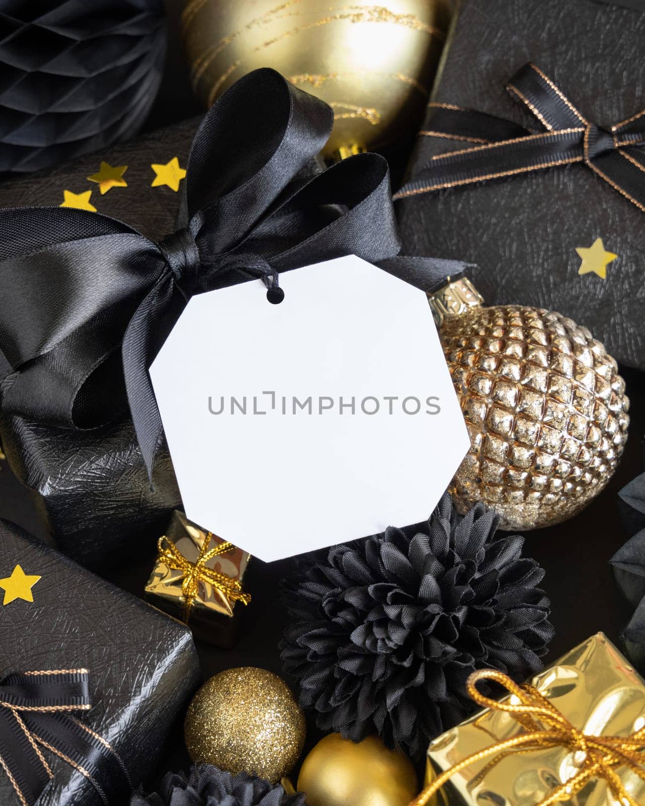 Black and golden Christmas Gift Boxes with a bow and ornaments close up, square paper gift tag mockup, copy space. Dark winter composition with blank label card for Christmas, New Year, Birthday, Anniversary