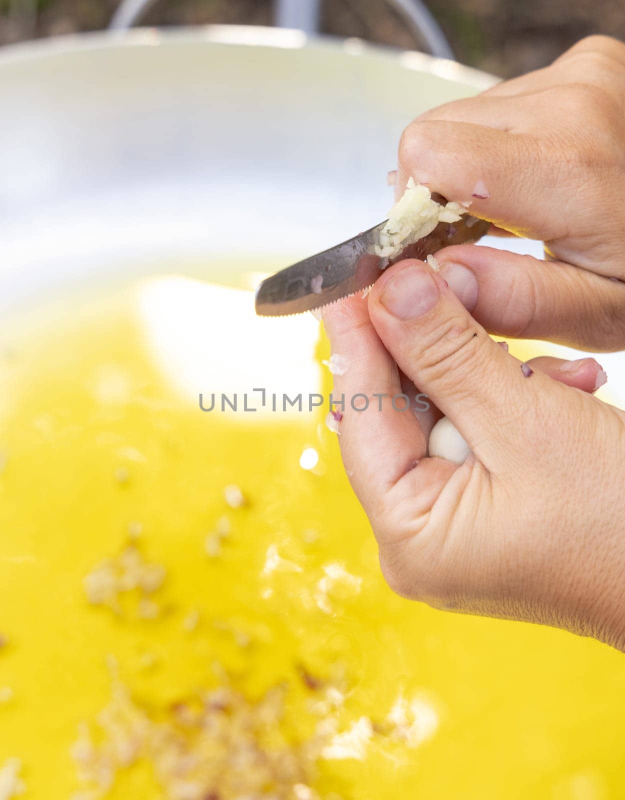 Woman hands chopping garlic clove over a big frying pan with olive oil close up, copy space. Traditional italian and apulian cousine, cooking for huge family