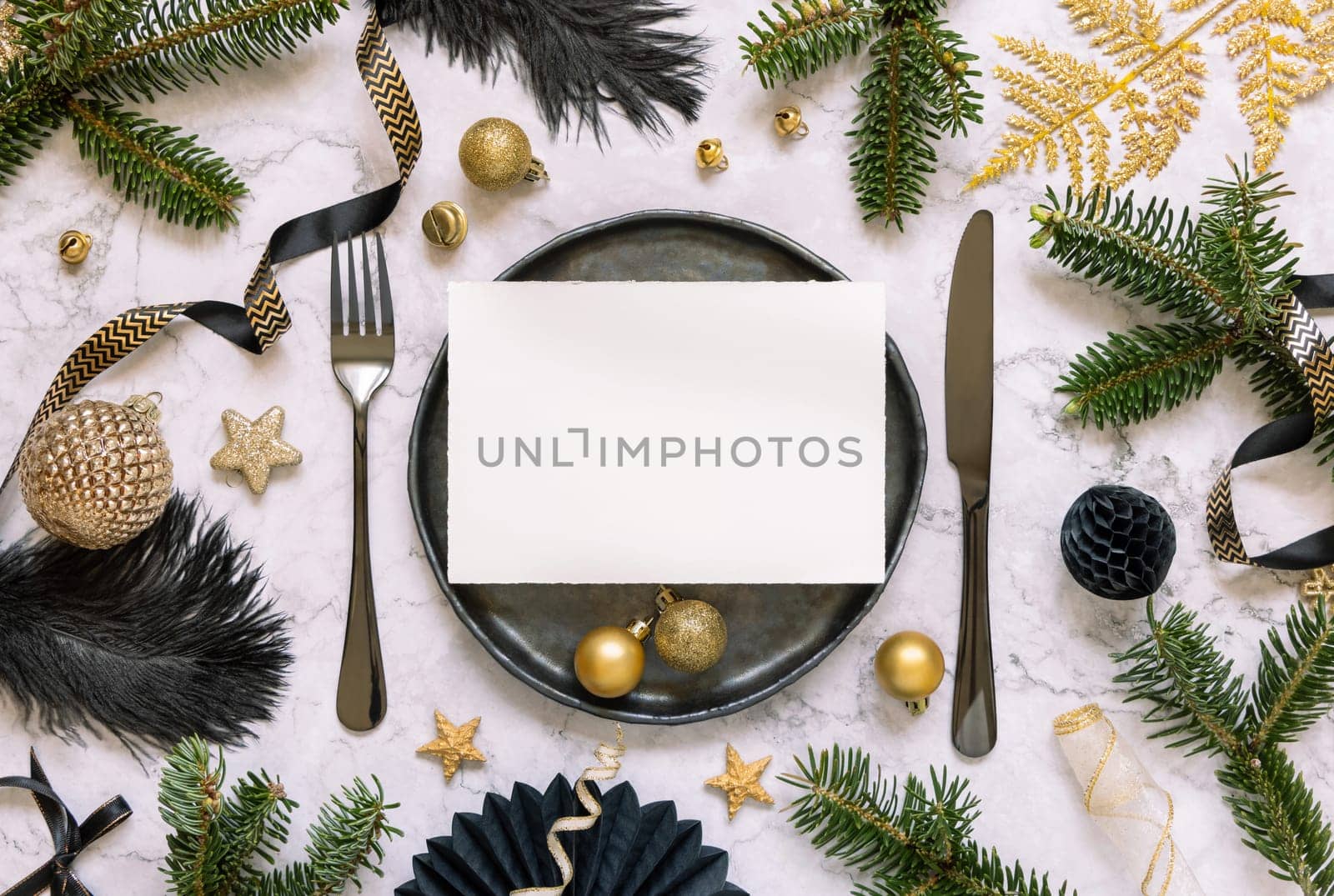 Black and golden Table setting with ornaments and fir tree branches top view, invitation card mockup. Christmas or New Year atmospheric composition on marble table, copy space.