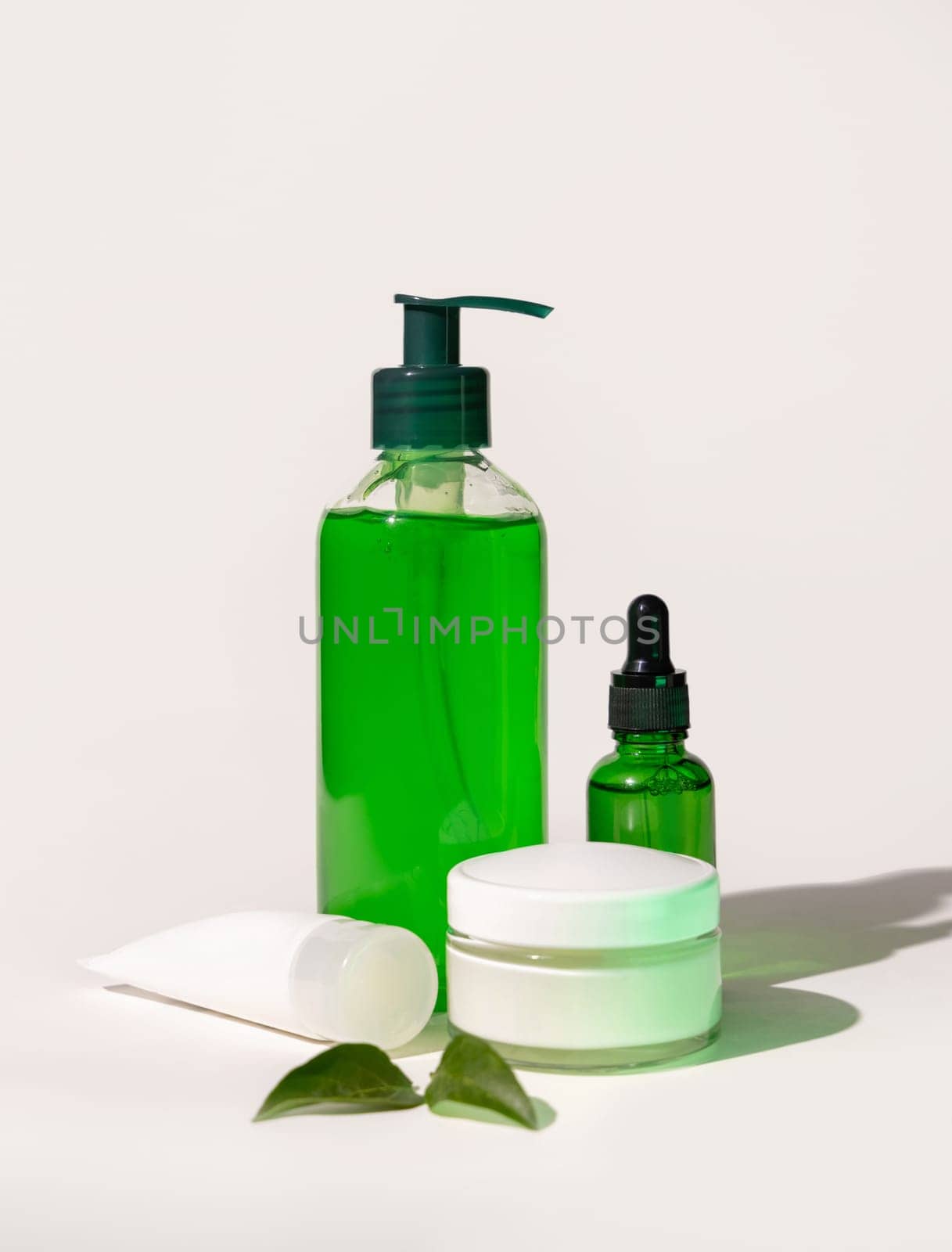 Refillable Cosmetic bottles, jar and tube near green leaves on white, bottles filled with green liquid, close up, mockup. Skincare beauty products. Natural cosmetics with aloe vera..