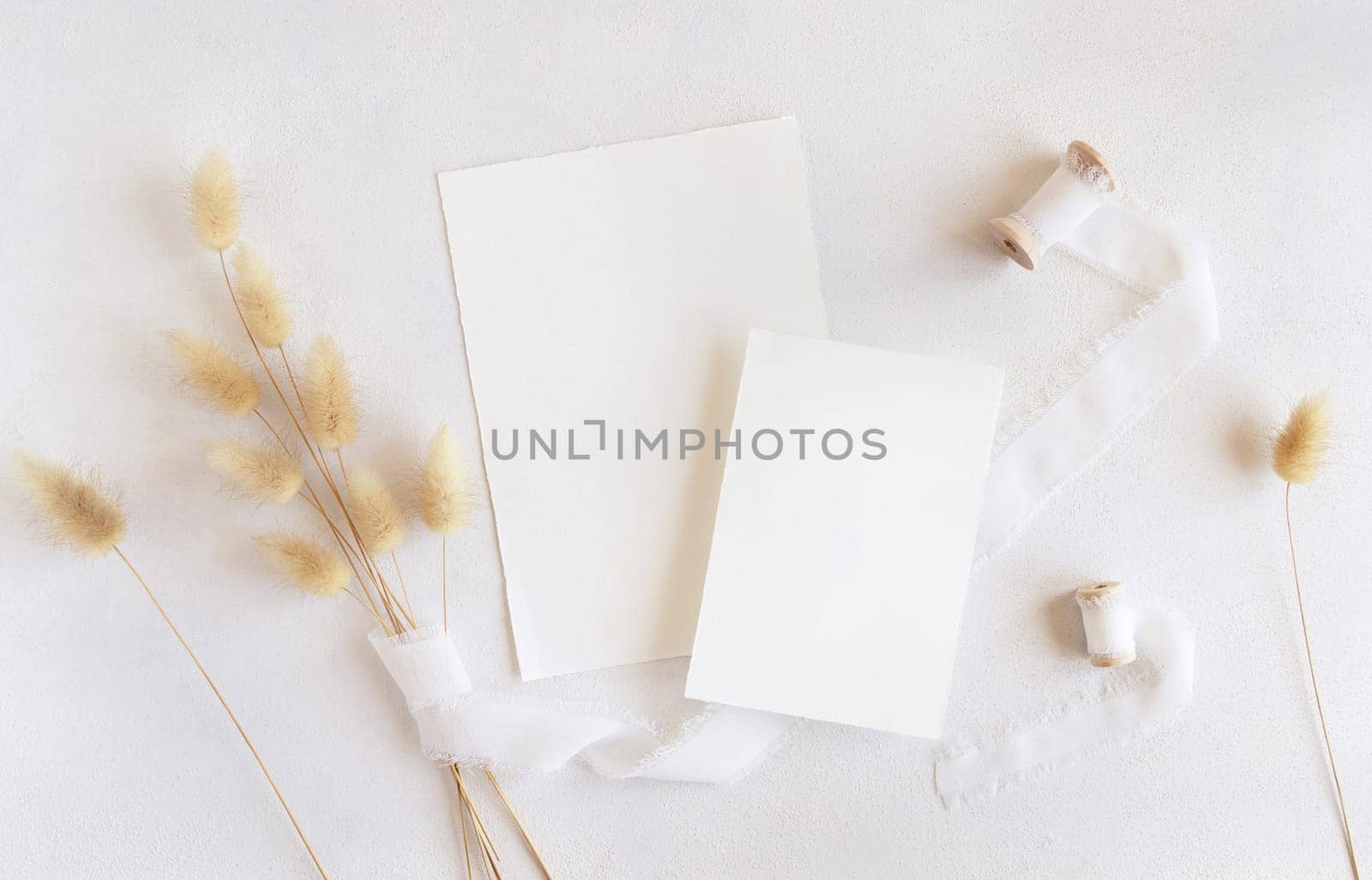 Blank cards near silk ribbons and dried hare's tail grass top view on white, mockup. Boho romantic scene with vertical cards. Bohemian or close to nature greeting or wedding Invitation