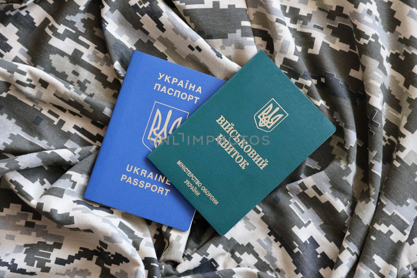Ukrainian military ID and foreign passport on fabric with texture of pixeled camouflage. Cloth with camo pattern in grey, brown and green pixel shapes with Ukrainian army personal token and passport.