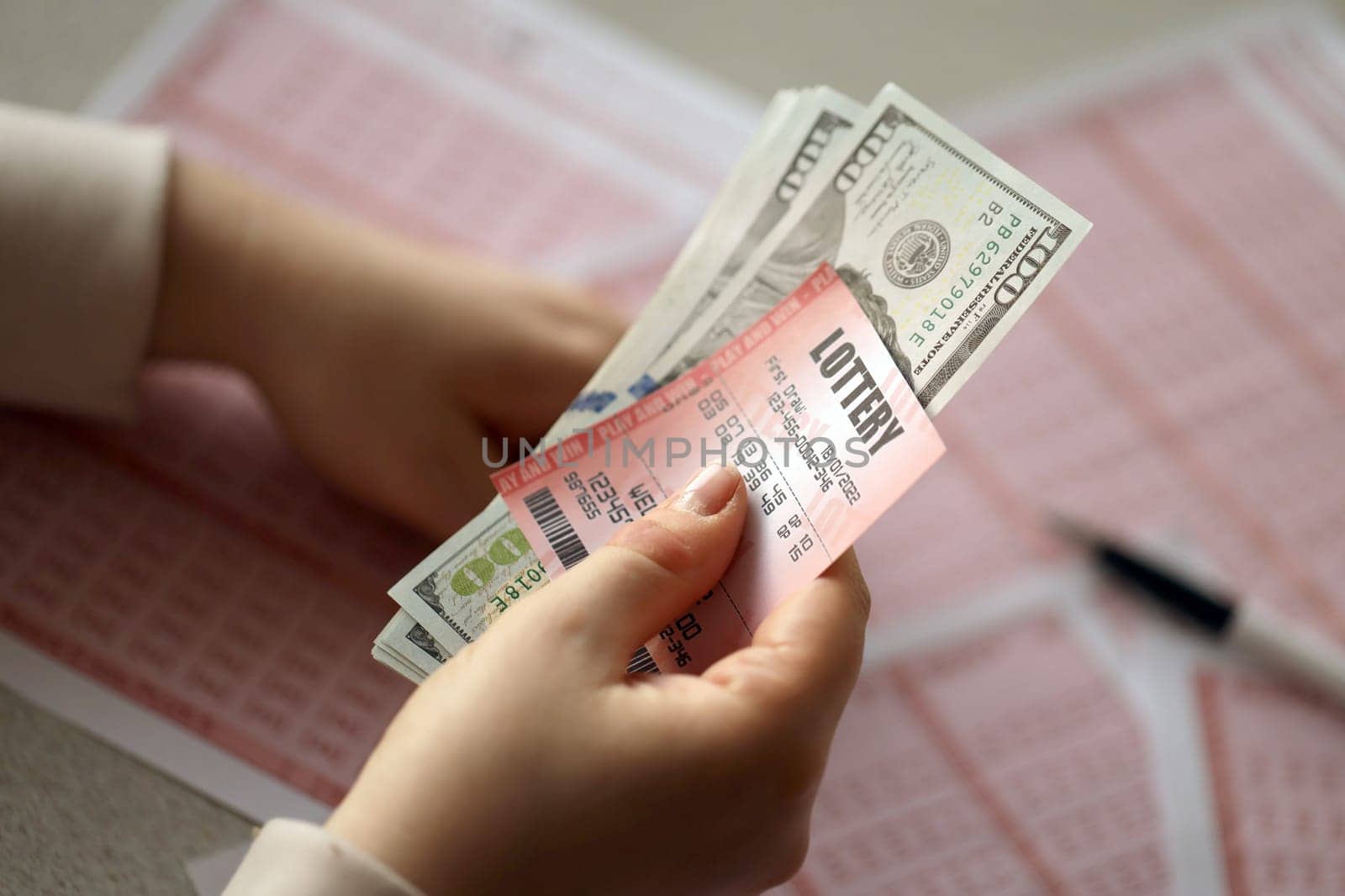 A young woman holds the lottery ticket with complete row of numbers and dollar bills on the lottery blank sheets background. Lottery winner concept