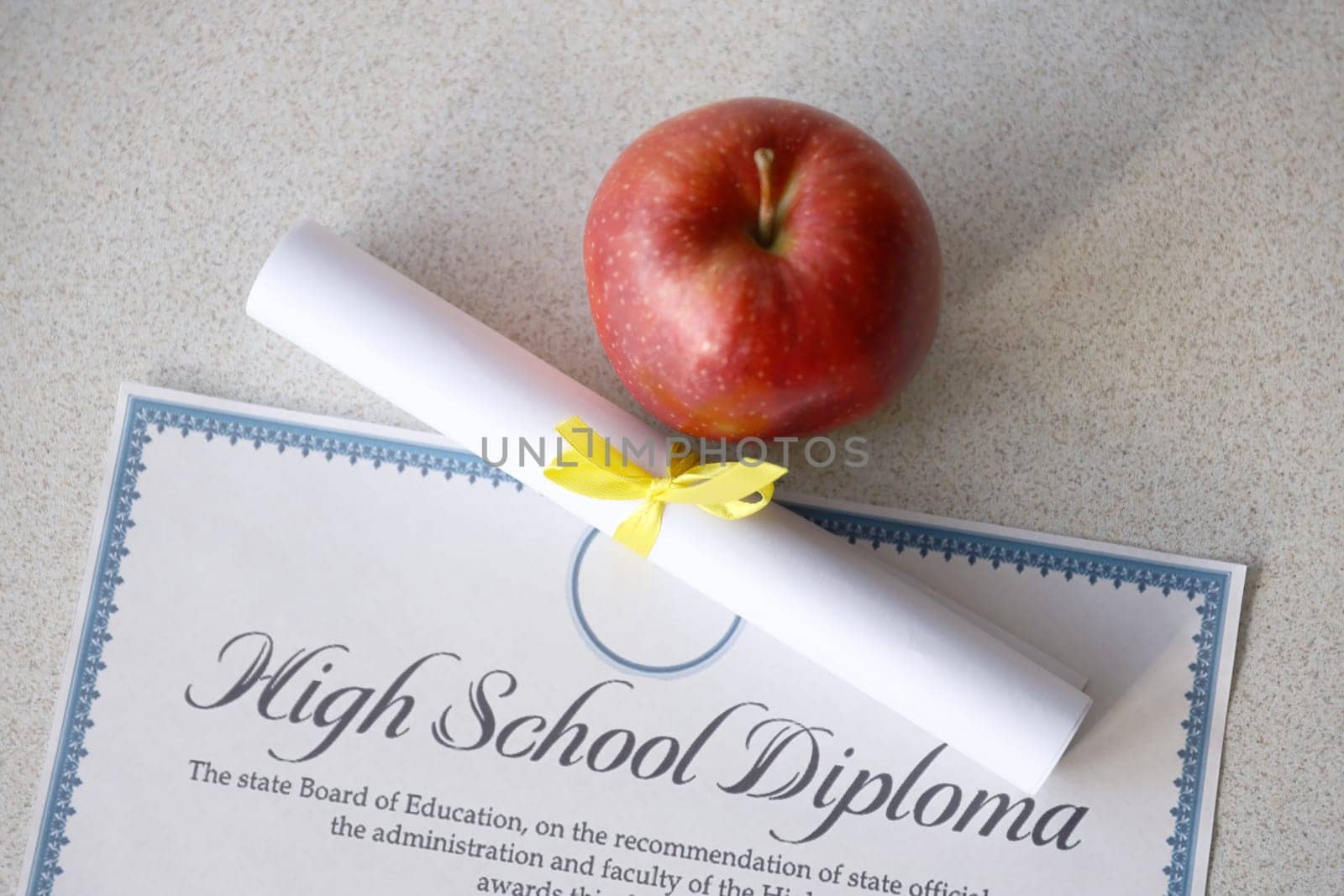 A high school diploma lies on table with small scroll and red apple. Education documents close up