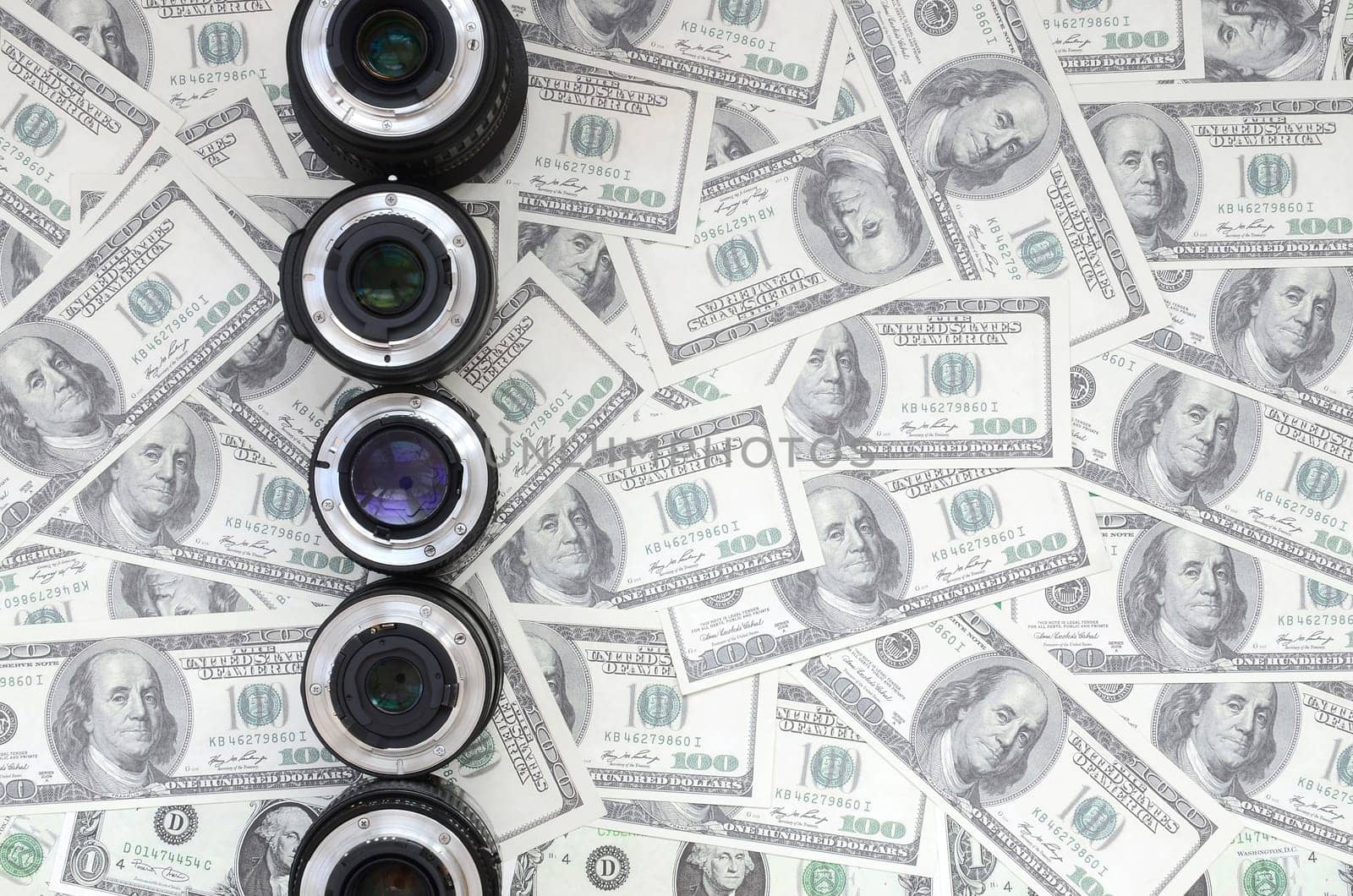 A few photographic lenses lies on the background of a lot of dollar bills. Space for text