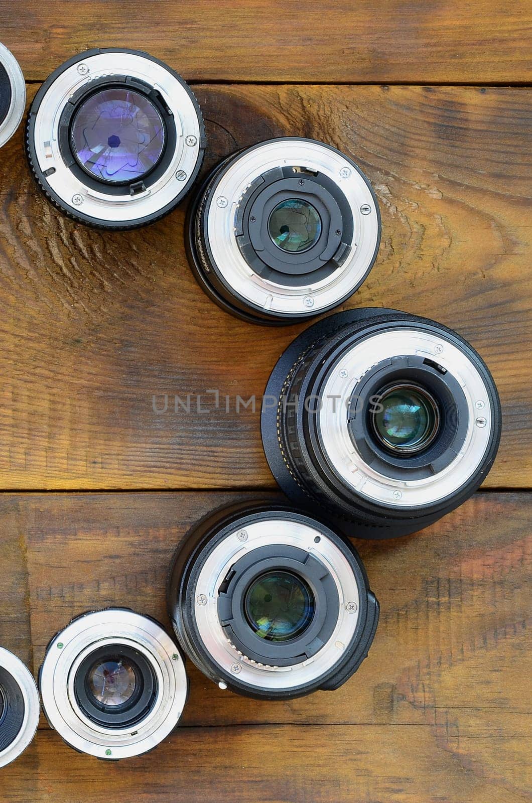 Several photographic lenses lie on a brown wooden background. Space for text