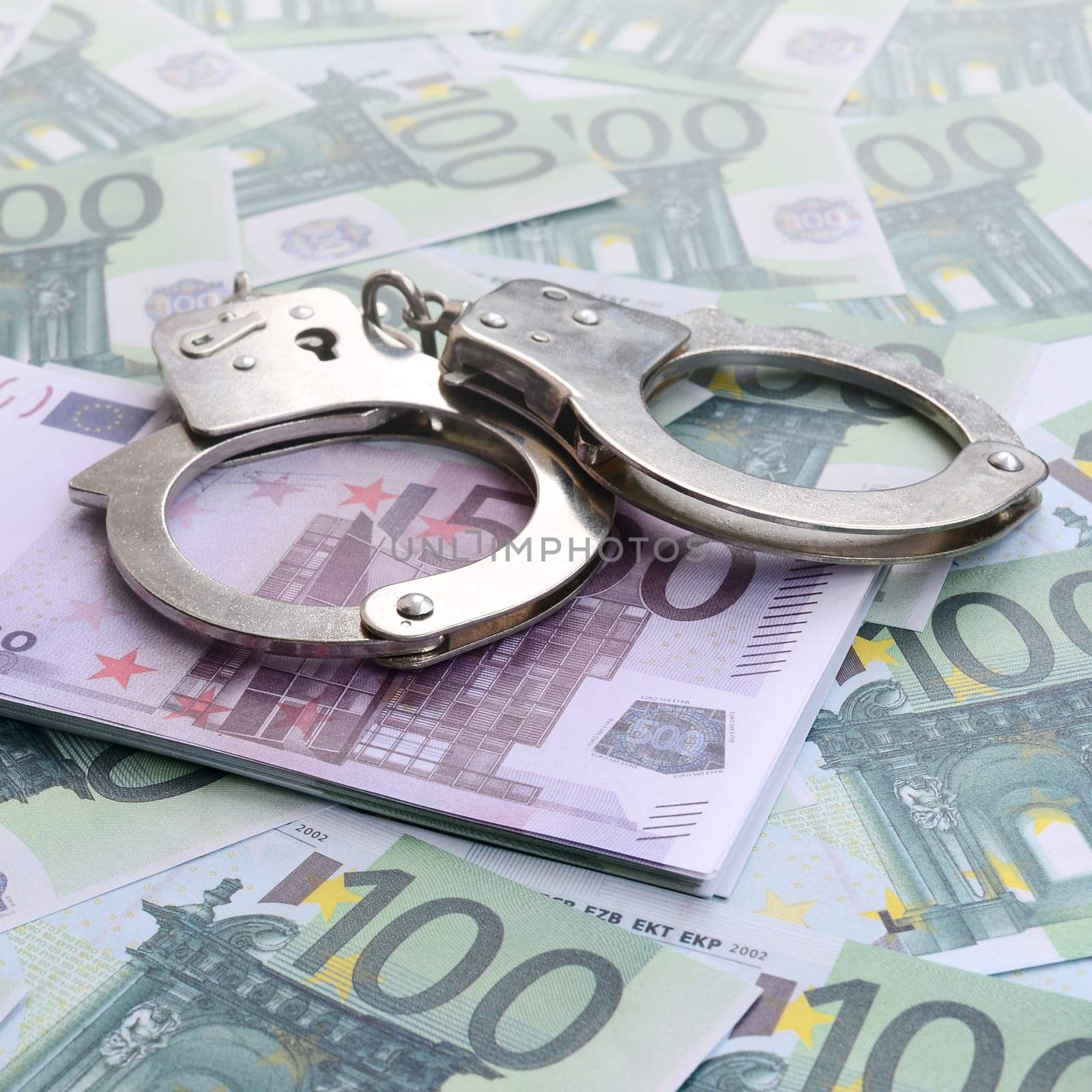 Police handcuffs lies on a set of green monetary denominations of 100 euros. A lot of money forms an infinite heap