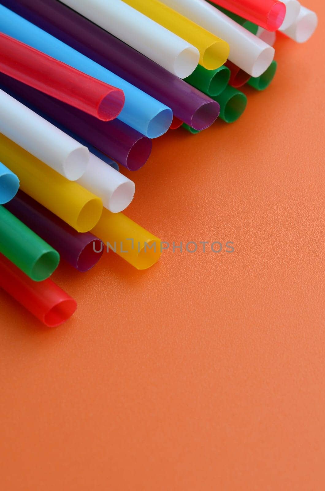 Many colorful straws for drinks lies on a bright orange background surface
