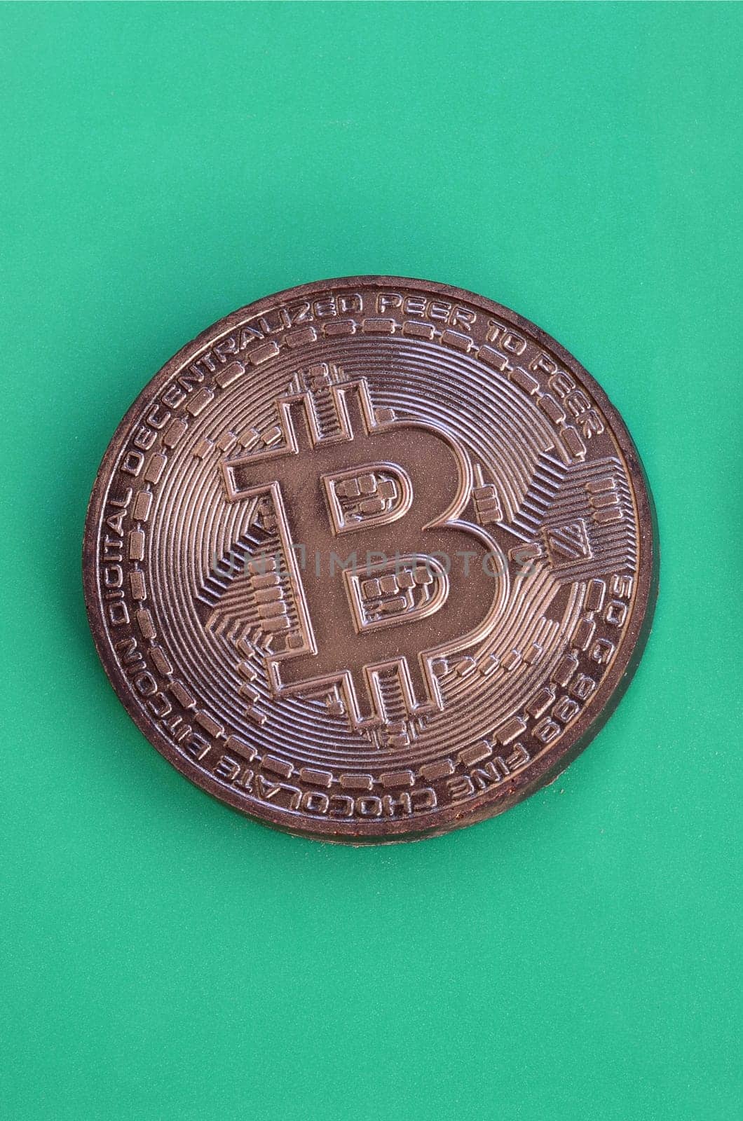 Chocolate product in the form of physical bitcoin lies on a green plastic background. Model of the crypto currency in the edible form