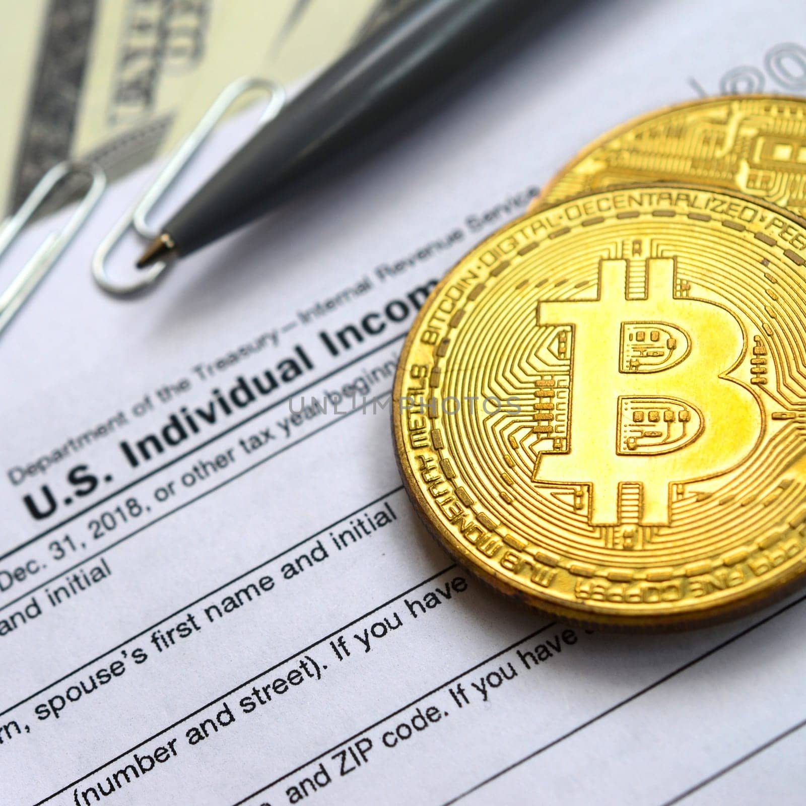 The pen, bitcoins and dollar bills is lies on the tax form 1040 U.S. Individual Income Tax Return. The time to pay taxes