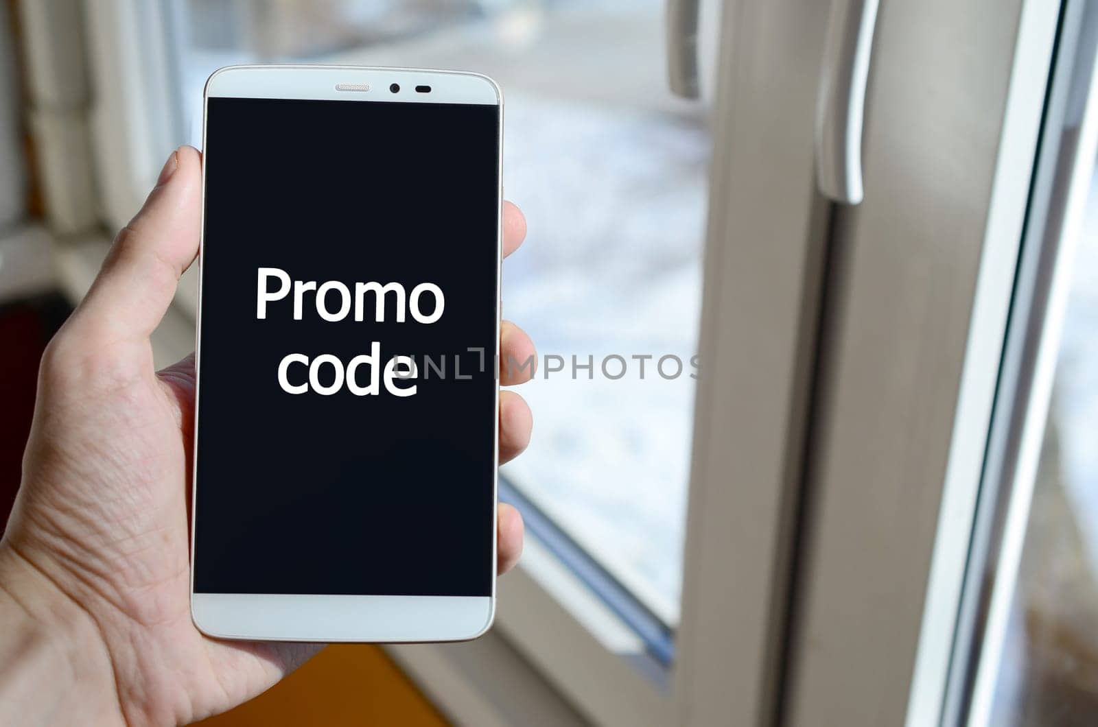 A person sees a white inscription on a black smartphone display that holds in his hand. Promo code