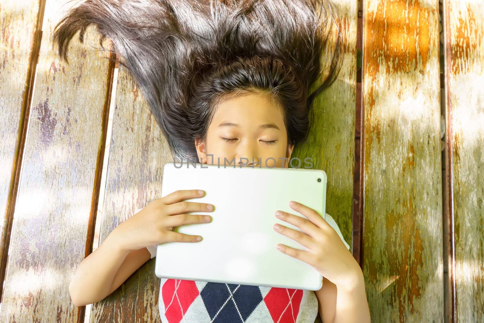 The girl sleep while playing tablet pc on wooden bed.