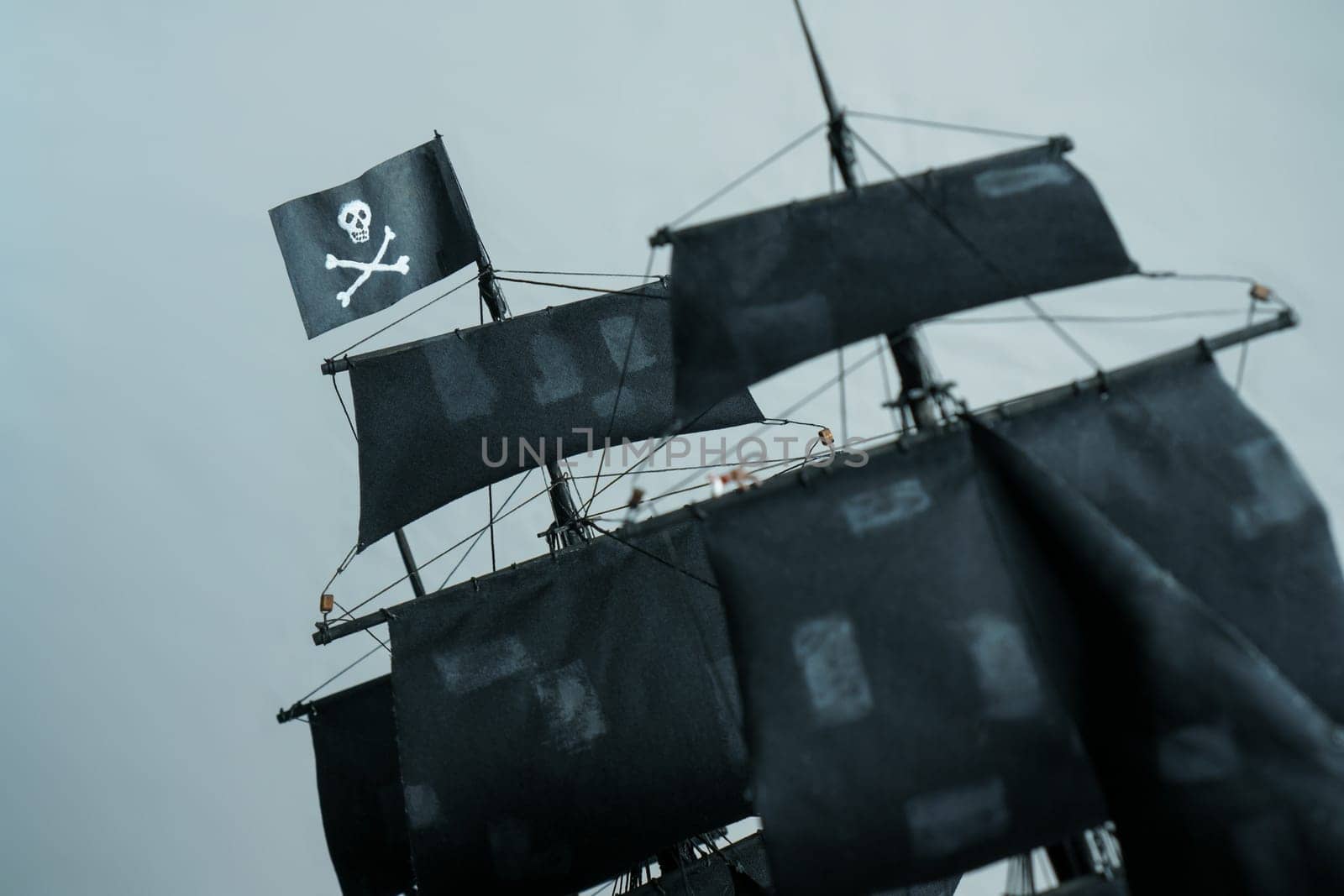 Close-up details of Pirate ship model Black pearl made of plywood. Flag Jolly Roger Skull and bones in focus, partially blurred patched sails and ropes