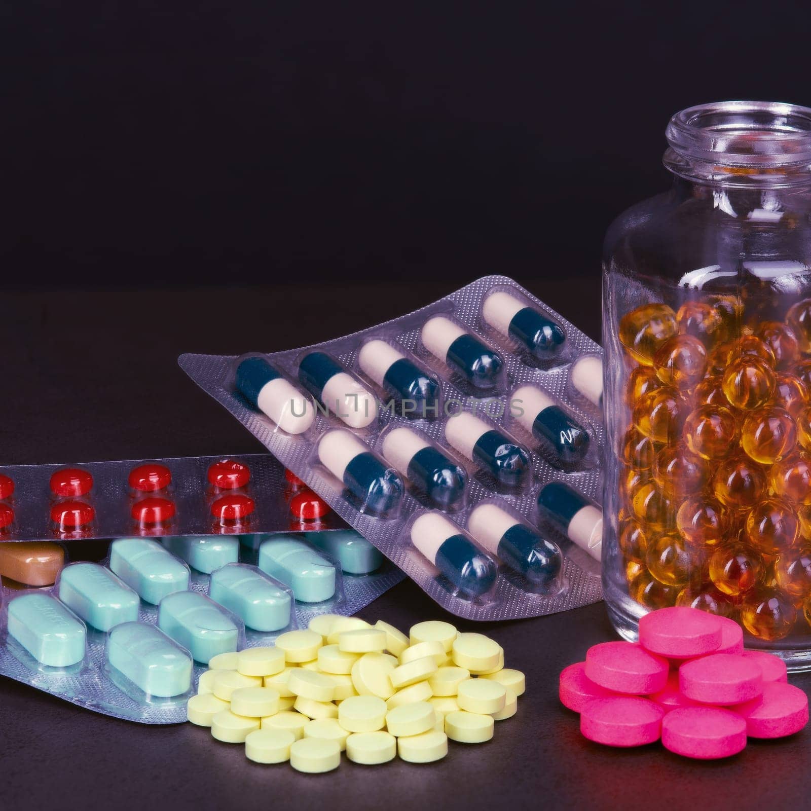 Pills and tablets of different colors are scattered and in bottles on a dark background