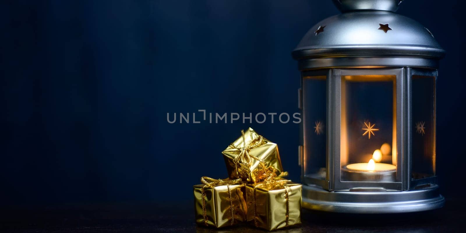 Christmas composition: lantern with candles, bright shiny gift boxes, dark blue background, place for logo, lettering, layout, layout.