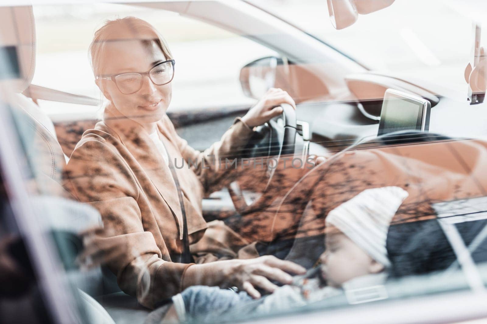 Mother concentrating on driving family car running errands while her baby sleeps in infant car seat by her site