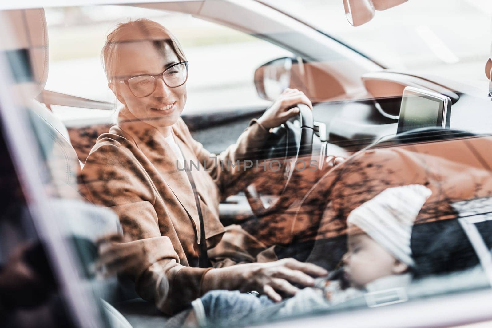 Mother driving family car, running errands, while her baby sleeps in infant car seat by her site