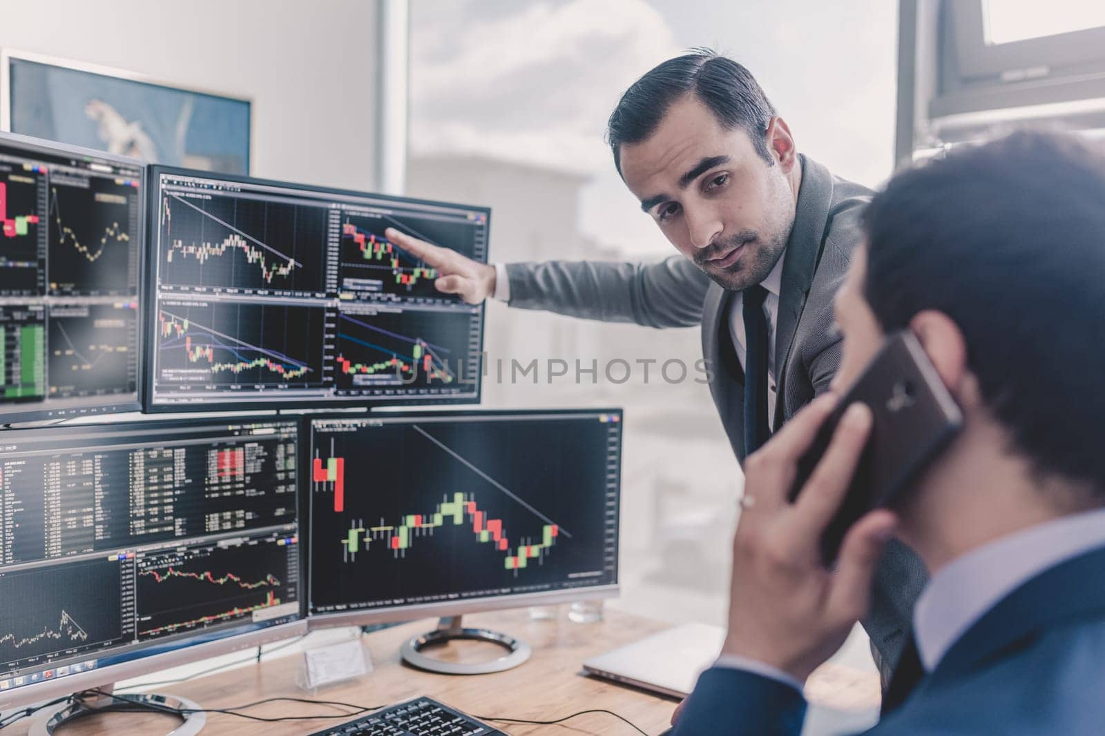 Businessmen trading stocks online. Stock brokers looking at graphs, indexes and numbers on multiple computer screens. Colleagues in discussion in traders office. Business success concept.