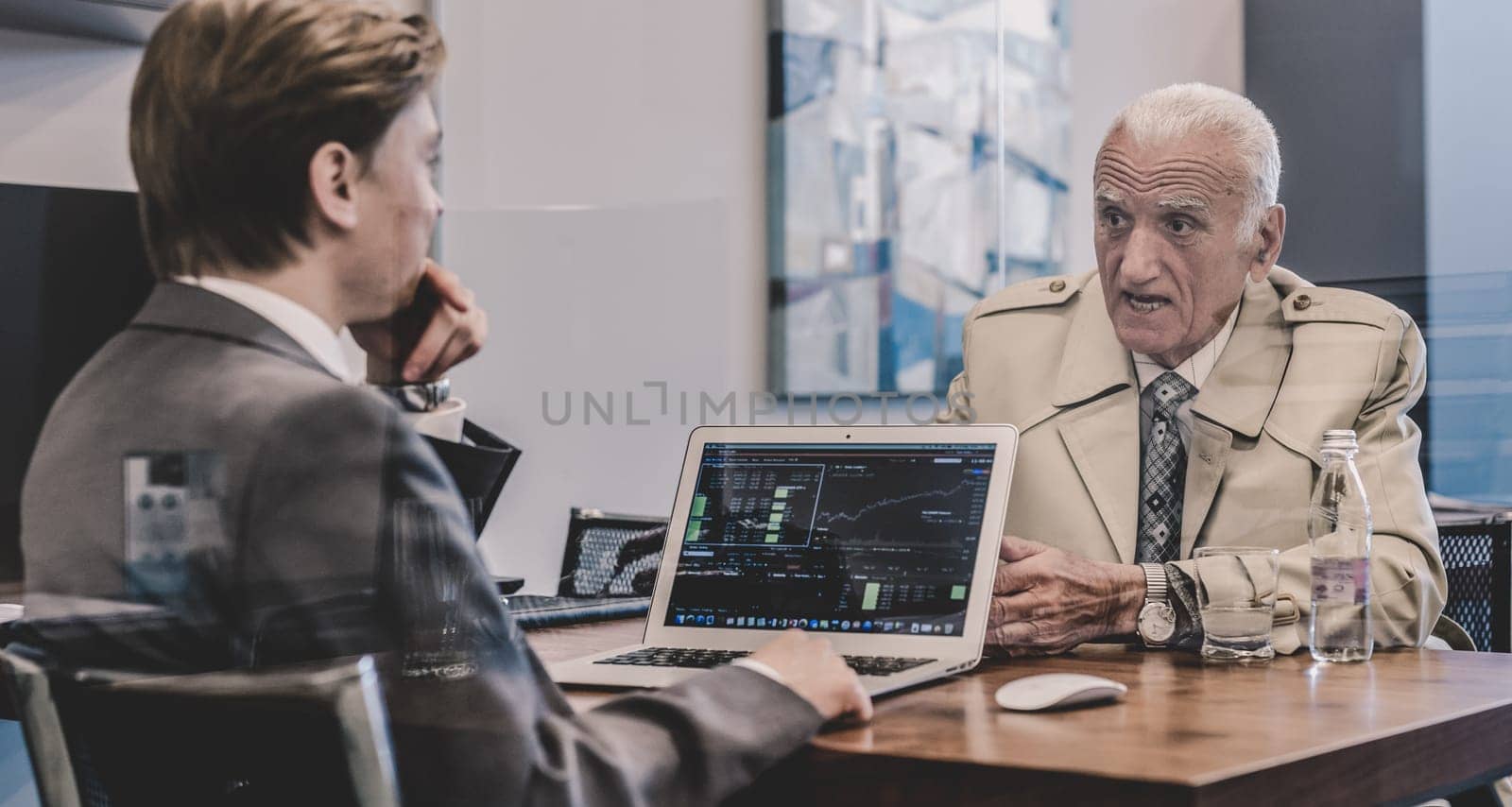 Young financial advisor sitting in front of laptop, consulting senior client with his investment strategy.
