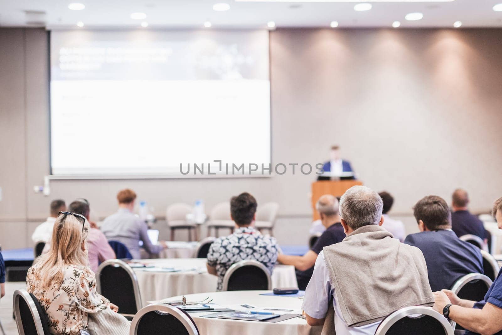 Speaker giving a talk in conference hall at business event. Rear view of unrecognizable people in audience at the conference hall. Business and entrepreneurship concept