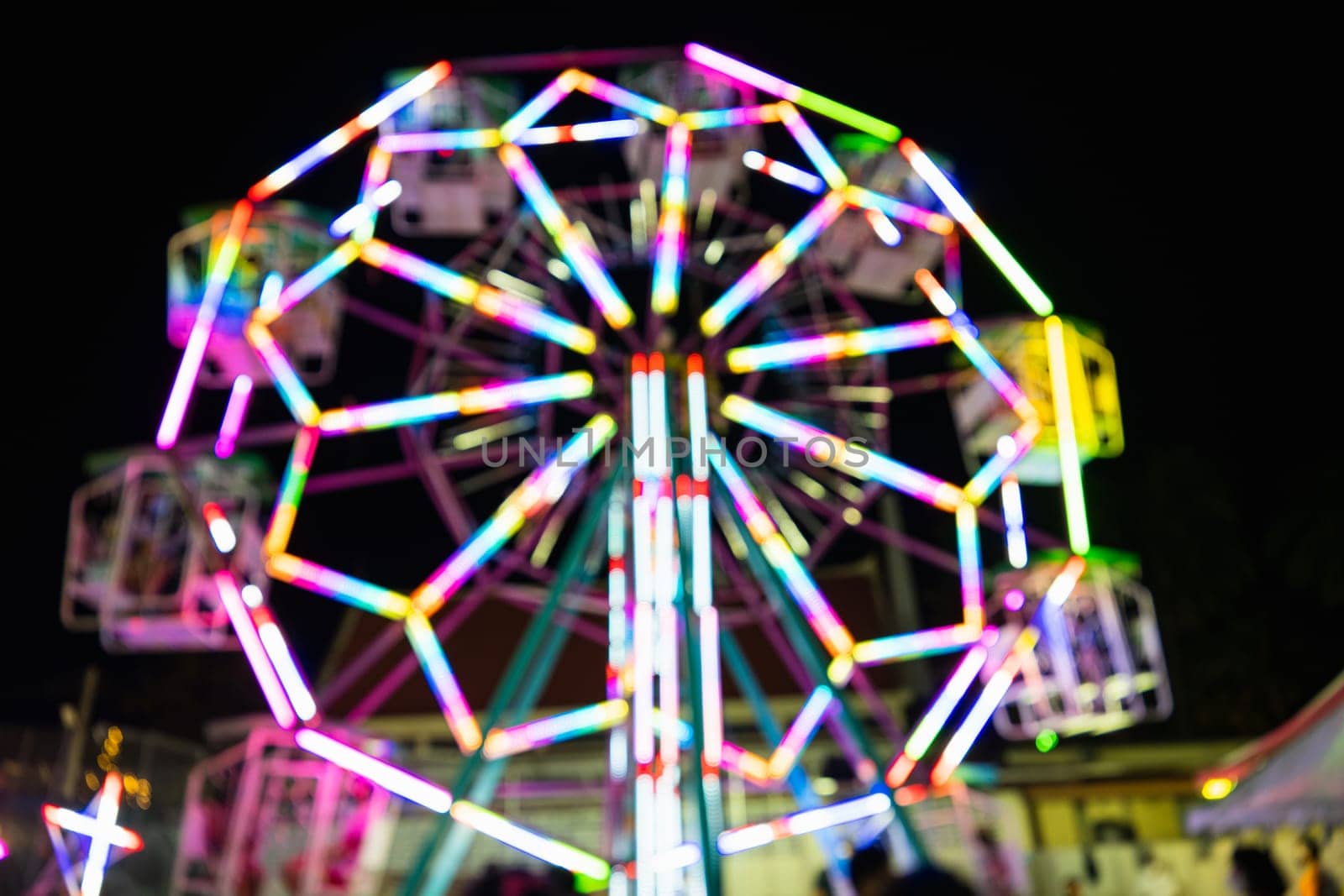 Blurry rollercoaster in bokeh, Ferris wheel at night of colorful with outdoor, Defocused (blurred) and blur image of Amusement park, The annual temple event has activities. Image out of focus