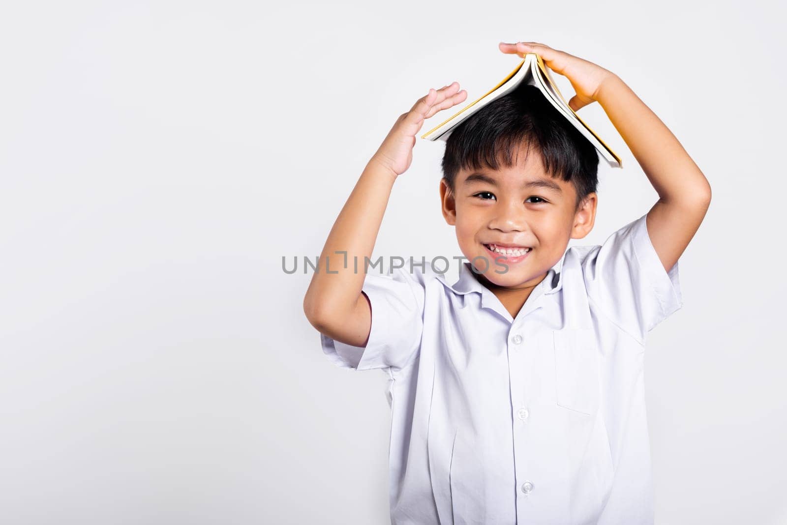 Asian adorable toddler smiling happy wearing student thai uniform red pants stand holding book over head like roof in studio shot isolated on white background, Portrait little children boy preschool