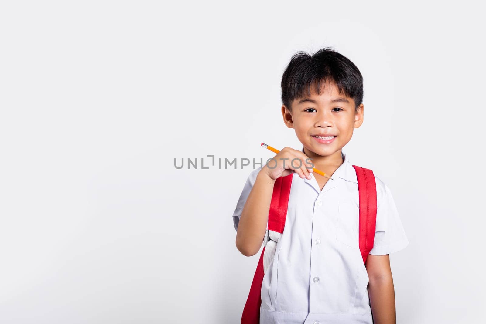 Asian toddler smiling happy wear student thai uniform red pants holding pencil for writers notebook in studio shot isolated on white background, Portrait little children boy preschool, Back to school