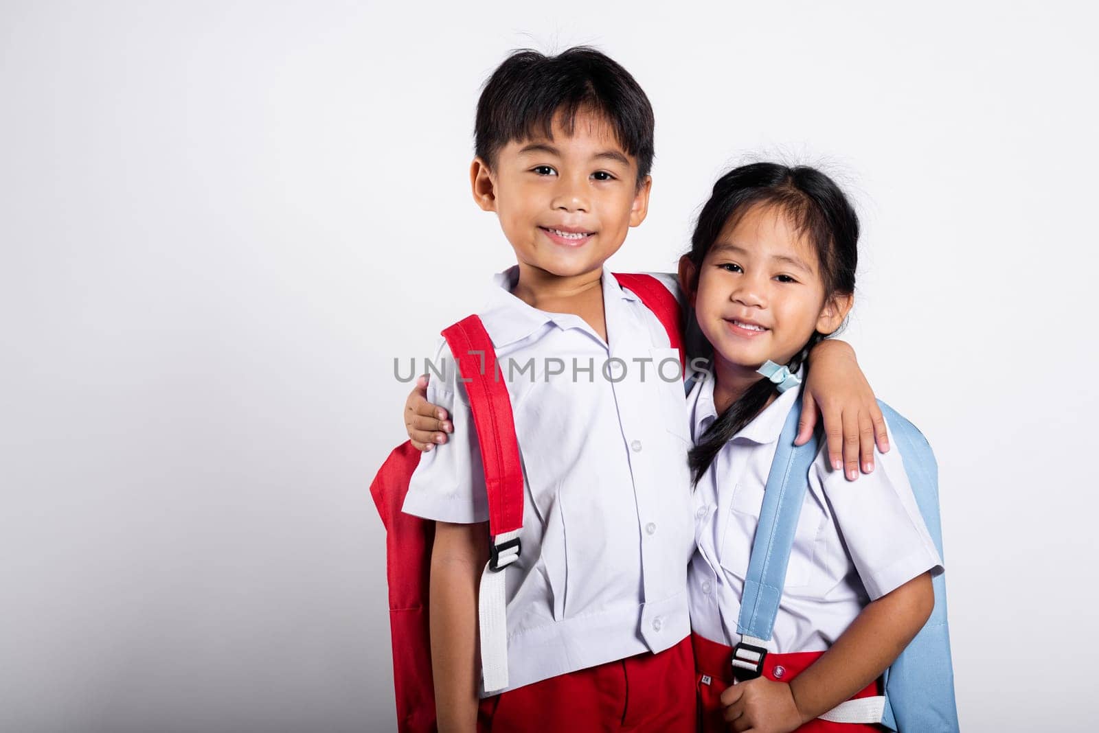 Two Asian student kid girl boy schoolchildren brother sister smile happy wear student thai uniform red pants skirt hug each other isolated on white background, Portrait little children girl preschool