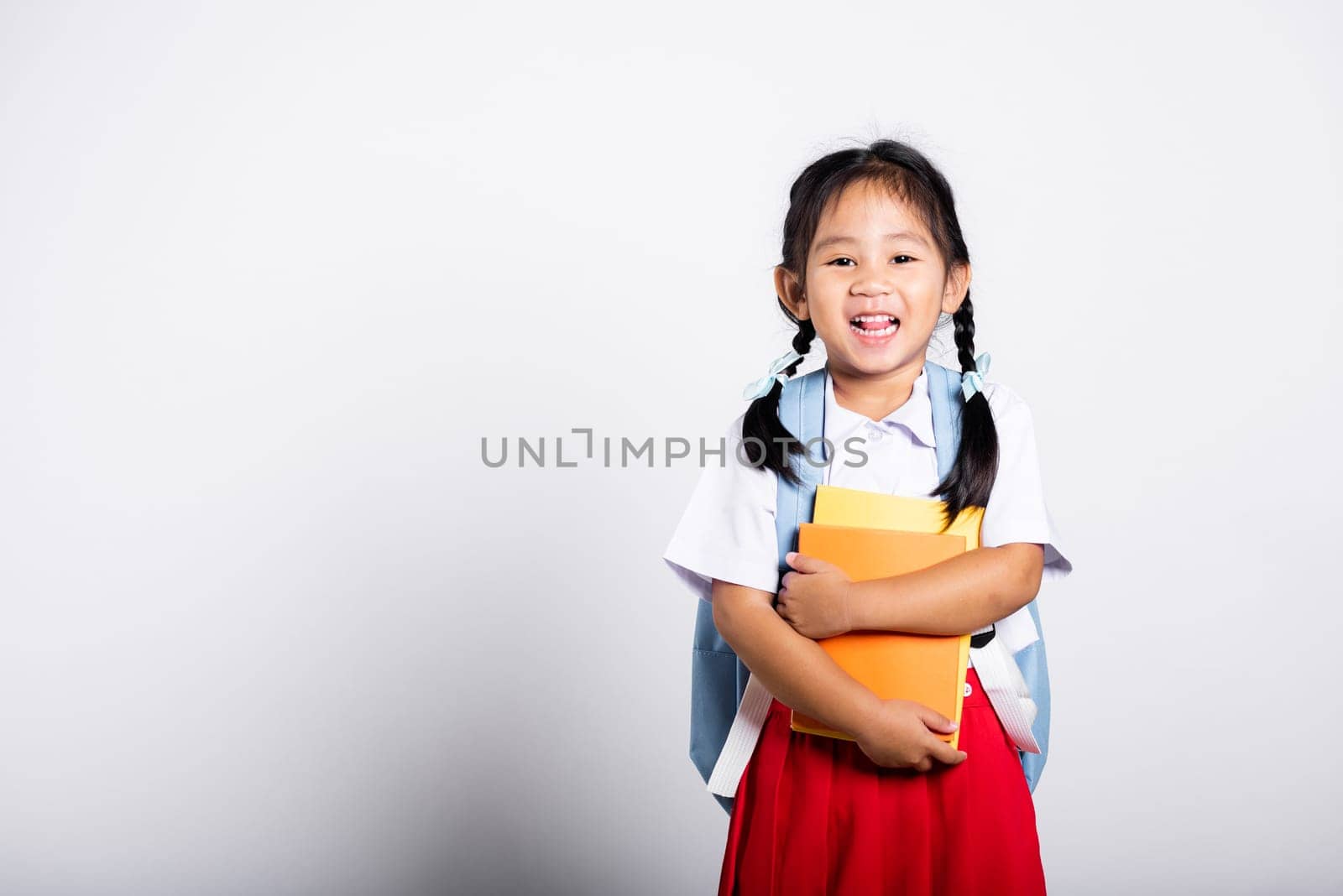 Asian adorable toddler smiling happy wear student thai uniform red skirt stand hold or hugging book in studio shot isolated on white background, Portrait little children girl preschool, Back to school