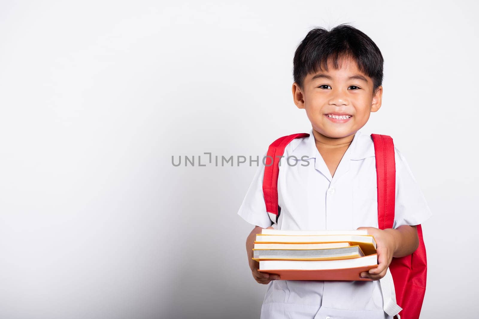 Asian adorable toddler smiling happy wearing student thai uniform red pants stand books for study ready for school isolated on white background, Portrait little children boy preschool, Back to school