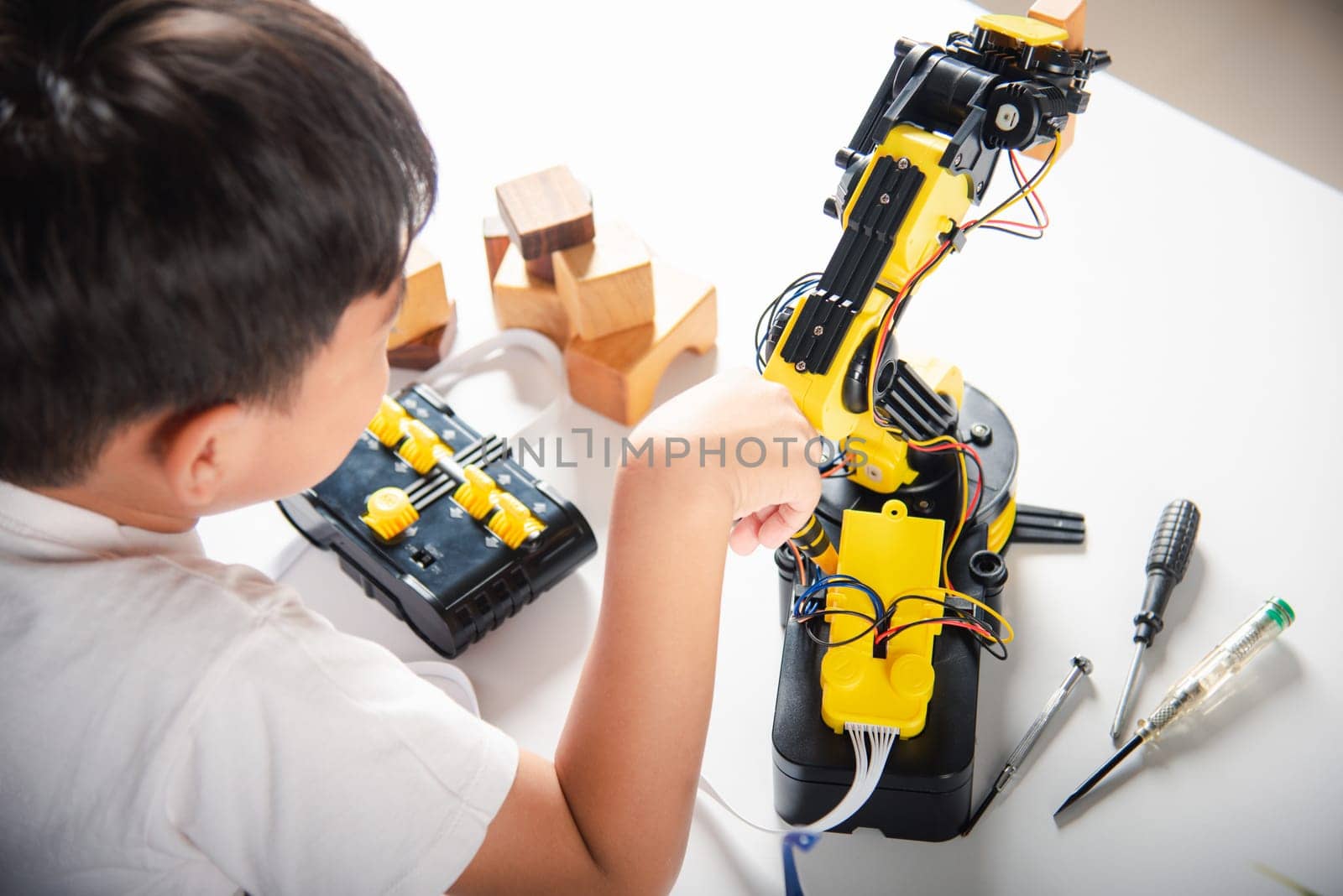 Happy Asian little kid boy using screwdriver to fixes screws robotic machine arm in home workshop, child learning repairing get lesson control robot arm, Technology future science education concept