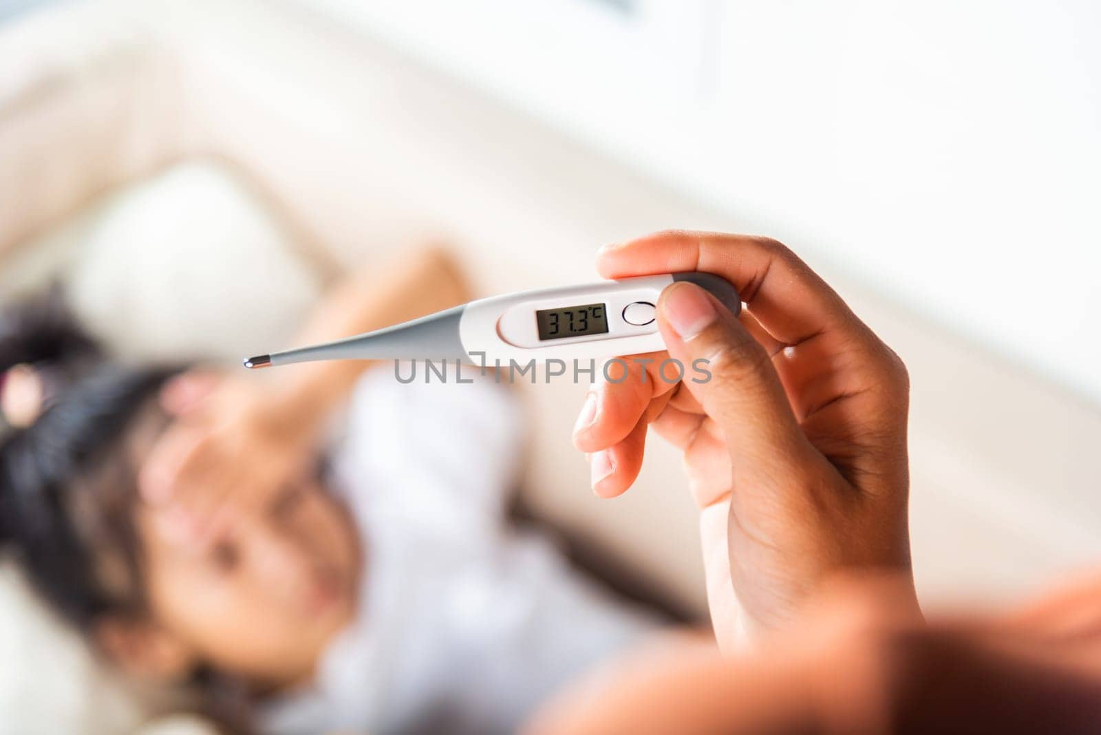 Sick kid. Mother checking temperature of her sick daughter with thermometer in mouth, child laying in bed taking measuring her temperature for fever and illness