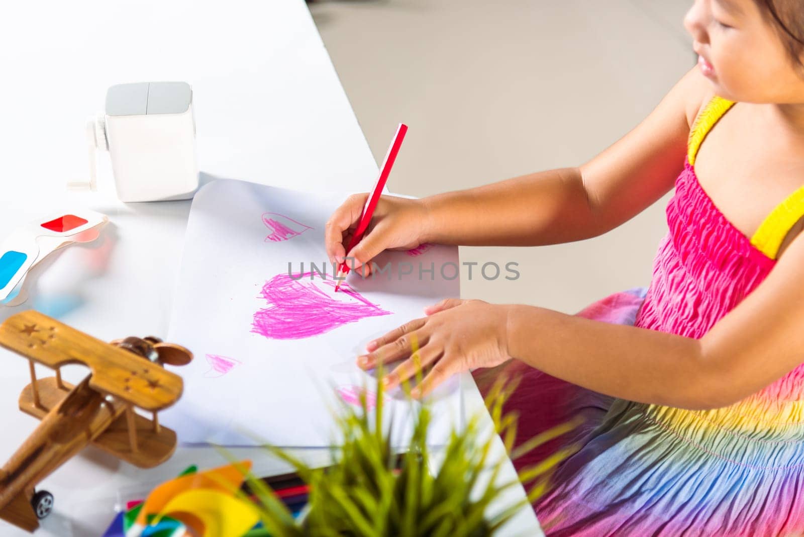 Happy child little girl colorful drawing pink heart on white paper, Asian cute kid preschooler smiling draw color love picture card at home, Valentine's or Mother's Day or Father's Day