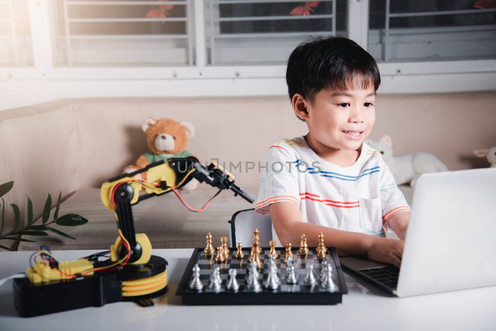 Asian little boy programming code to robot machine arm on laptop for play chess, STEM education E-learning, Funny children learning getting lesson control robot arm, Technology science education