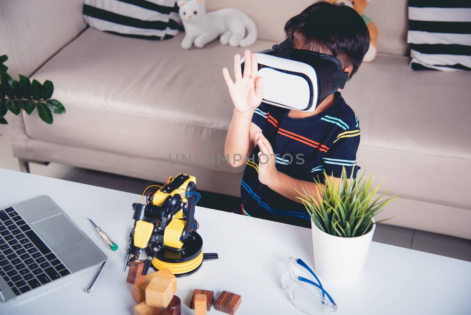 Virtual Reality Simulator. Asian kid boy using VR glasses on robotic arm in workshop, Child learning programer control robot arm with sensors to pick up wood block, Technology education. industry 4.0