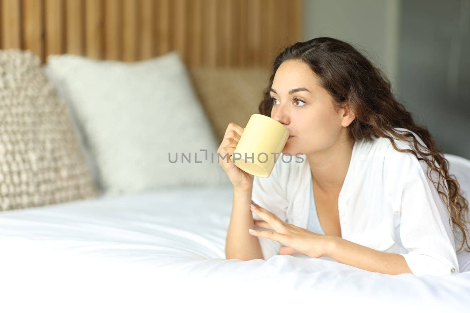 Woman drinking coffee lying on the bed in a bedroom