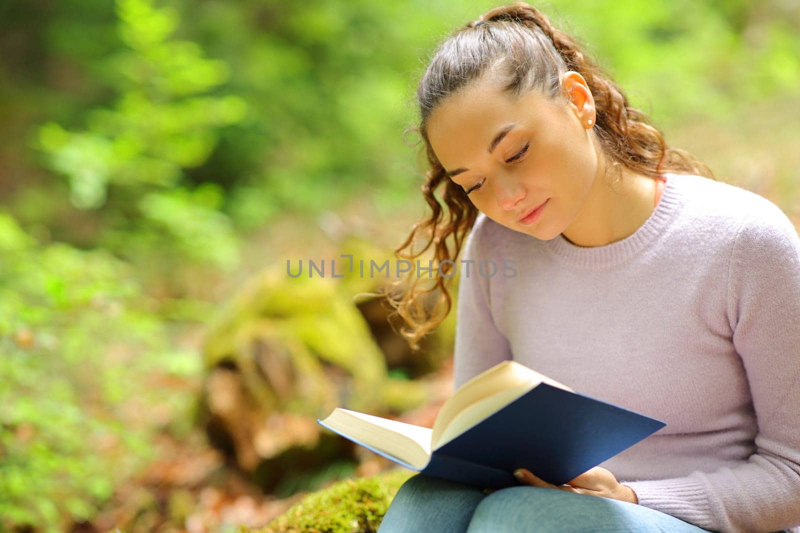 Concentrated woman reading a paper book sitting in nature